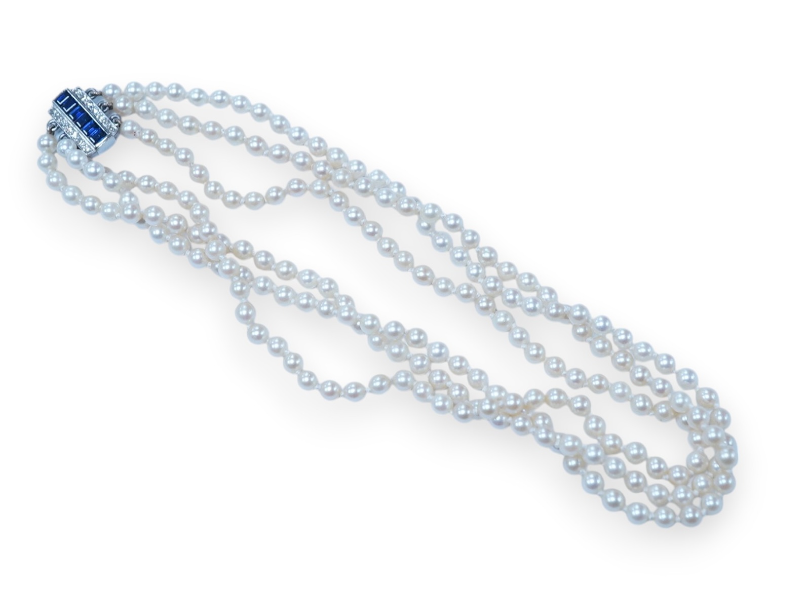 A triple strand cultured pearl choker necklace, with sapphire and diamond cluster set rectangular white metal clasp, 32cm. Condition - fair to good